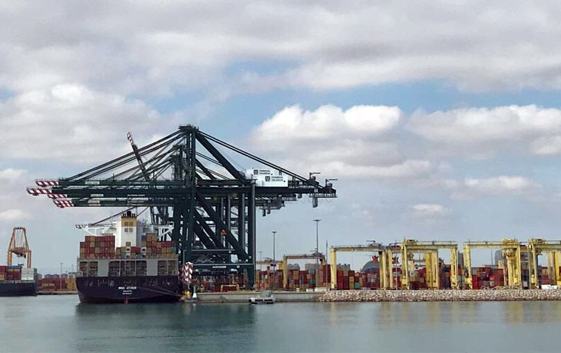 Fotografía de muelle de puerto con grúas de carga estibando un barco carguero